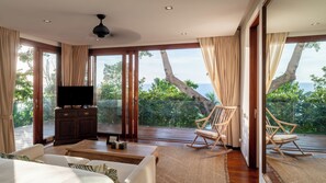 A spacious room with a large window, a flat-screen TV, a wooden cabinet, a rocking chair, and a sofa. - Villa Riva (Koh Samui)