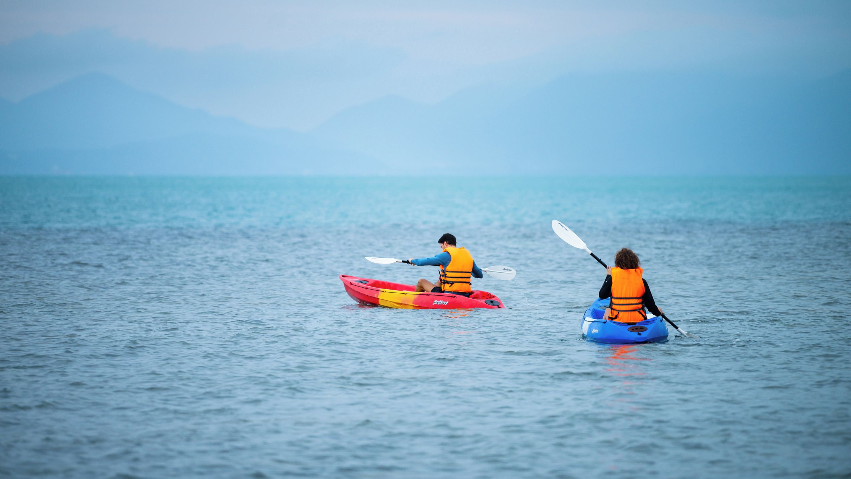 Two kayakers on a calm sea with distant mountains.