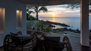 A balcony with wicker chairs and a view of the sunset over the sea.