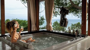 A person relaxing in a hot tub with a view of the ocean and trees. - Villa Riva (Koh Samui)