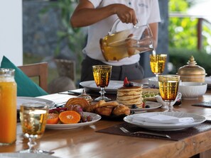 Ein Frühstücksbuffet mit Pfannkuchen, Früchten und Getränken auf einem Holztisch.