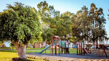 Explore the playground area surrounded by lush greenery and a serene body of water.
