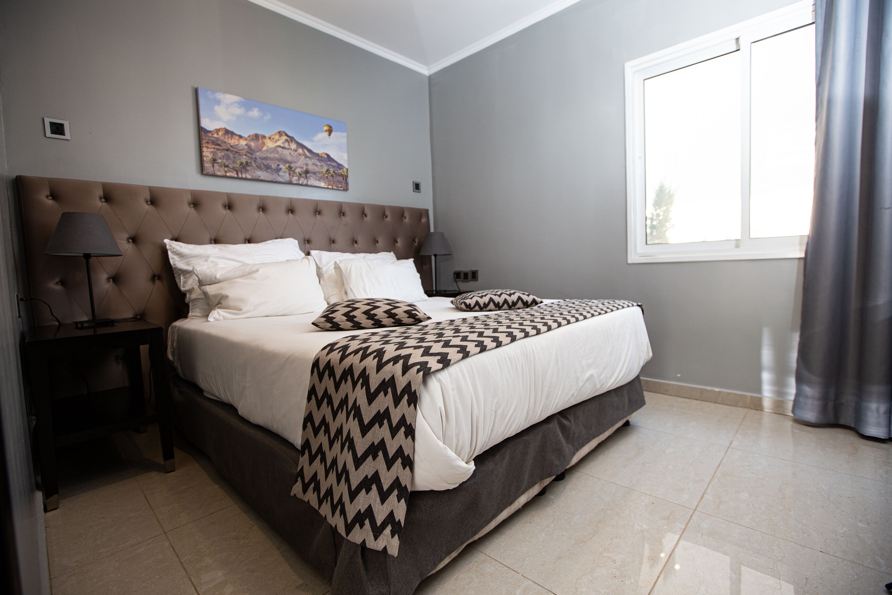 A neatly made bed with a patterned throw, a headboard, and a nightstand with a lamp.