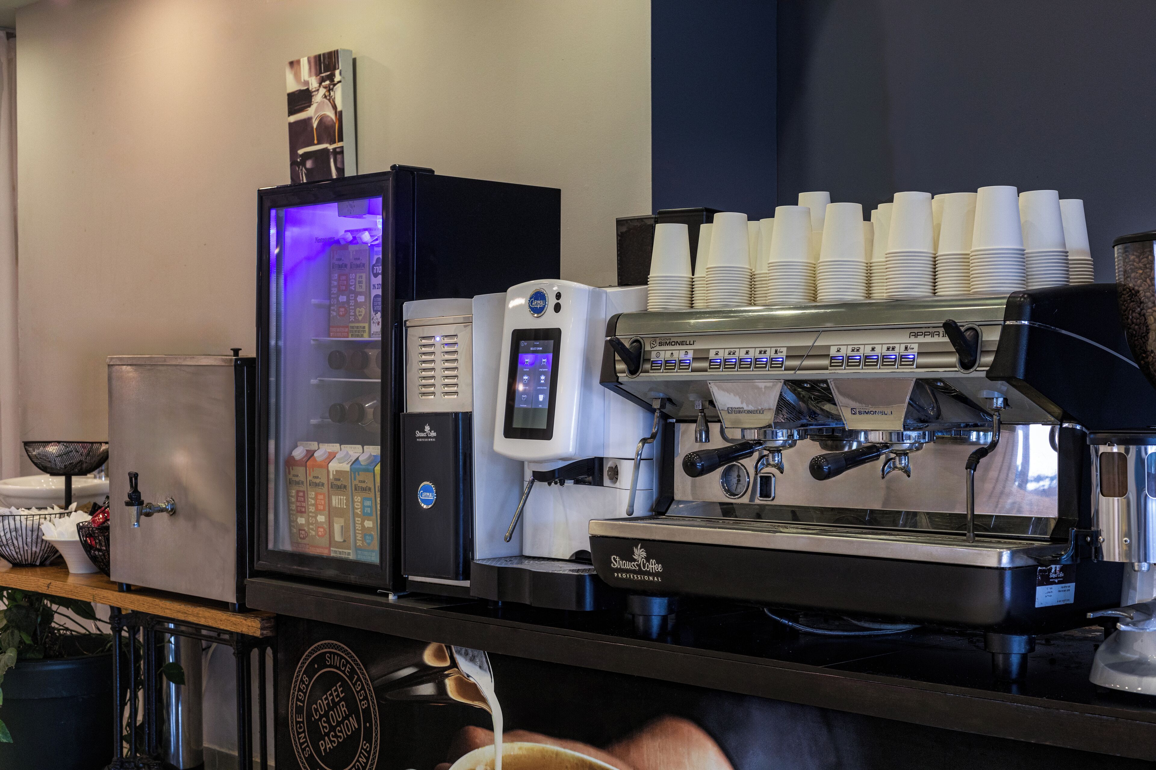 Una cafetera con varias tazas apiladas encima, un espumador de leche y un dispensador de café.