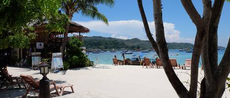 A beach with lounge chairs and a thatched-roof building.