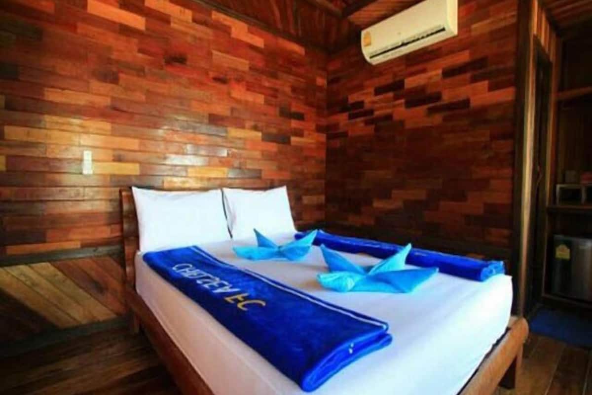 Una habitación con paneles de madera, una cama, almohadas y una toalla azul.