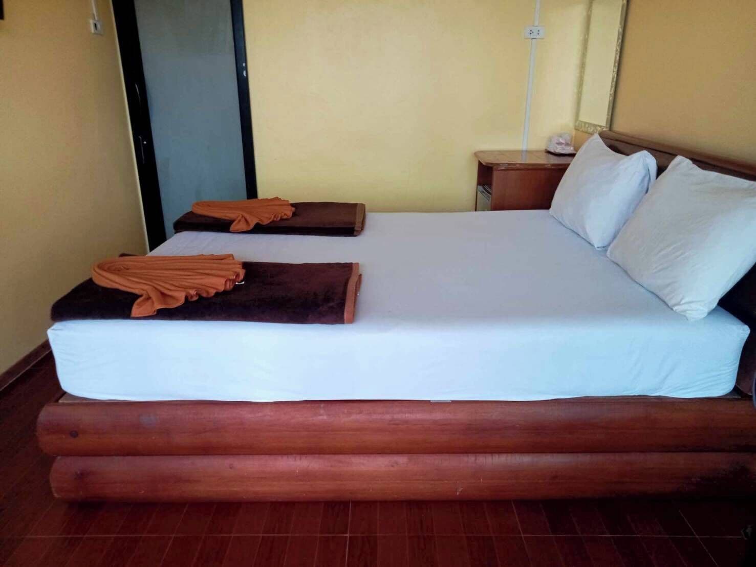 Une chambre d’hôtel avec un grand lit, une tête de lit en bois, une table de chevet avec une lampe et une porte.