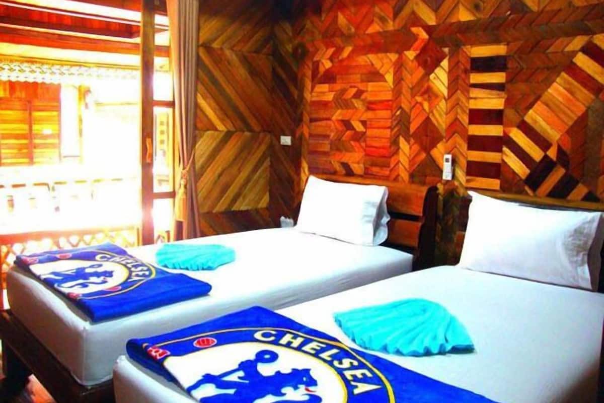 Habitación de hotel con dos camas, paredes de madera con diseño y una ventana con cortinas.