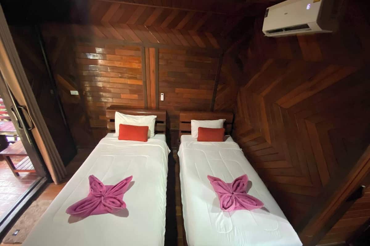 Una habitación con dos camas, cada una con ropa de cama blanca y cabeceros florales rosa. Un equipo de aire acondicionado está montado en la pared sobre las camas.