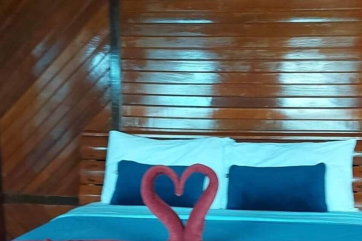 Una cama con una colcha azul y almohadas, y una toalla roja dispuesta en forma de corazón.