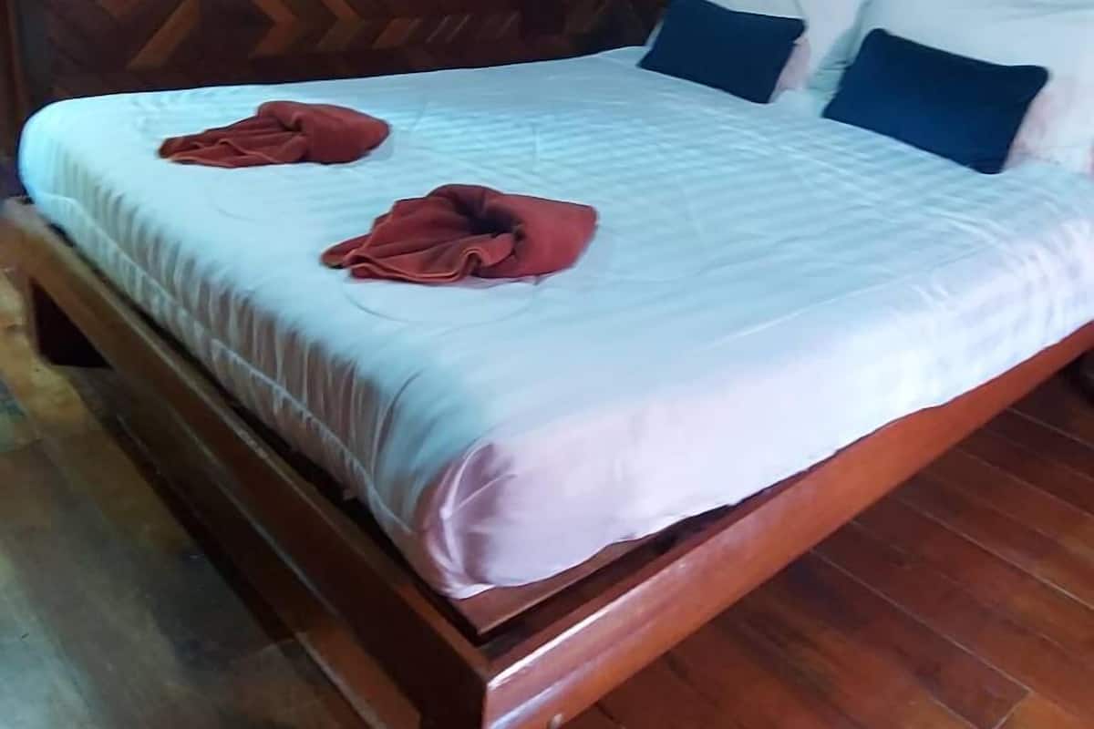 Una cama de madera con colchón blanco y dos almohadas, una colcha roja y un equipo de aire acondicionado encima.