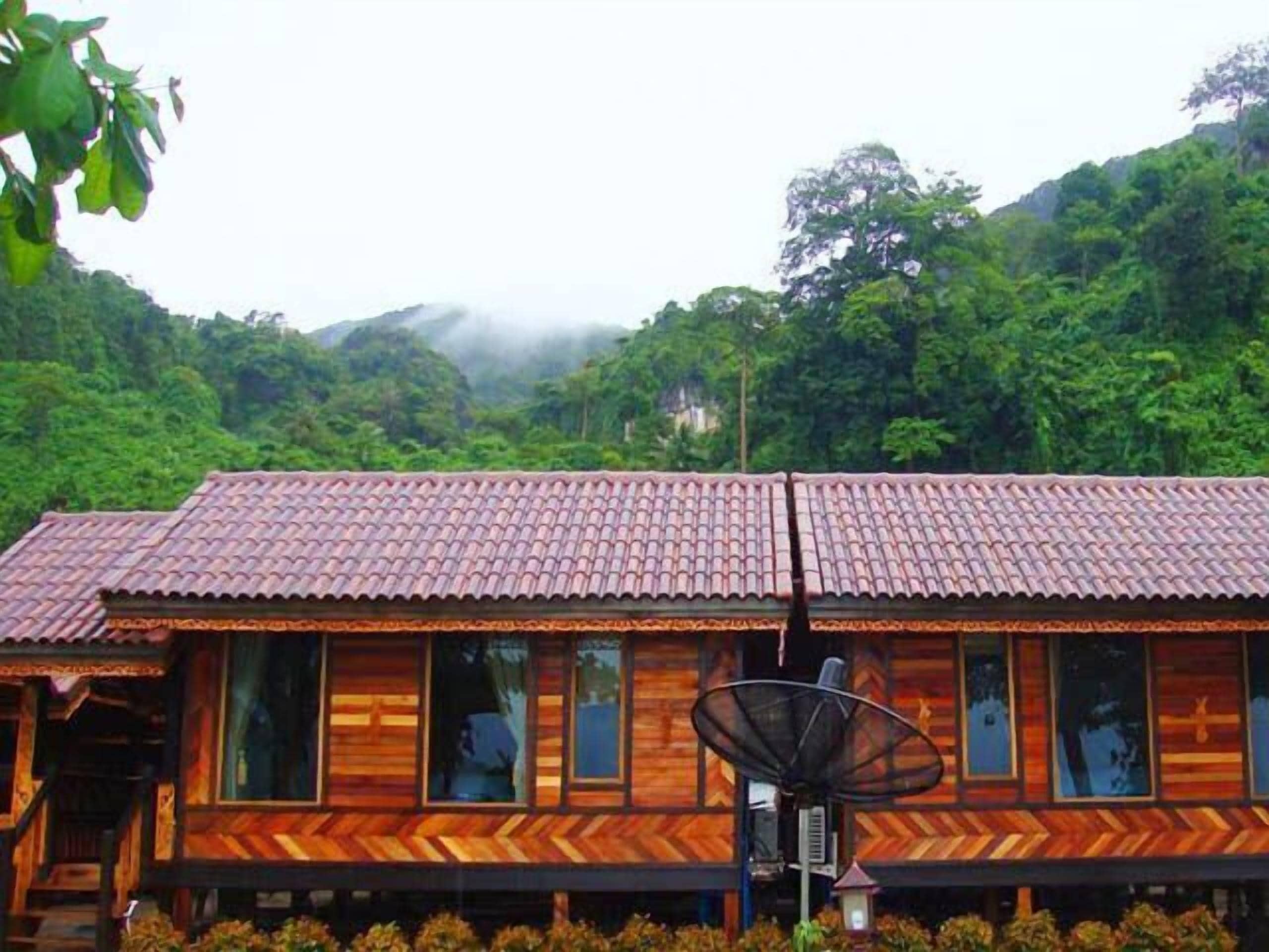 A wooden cabin with a tiled roof, large windows, and a satellite dish.