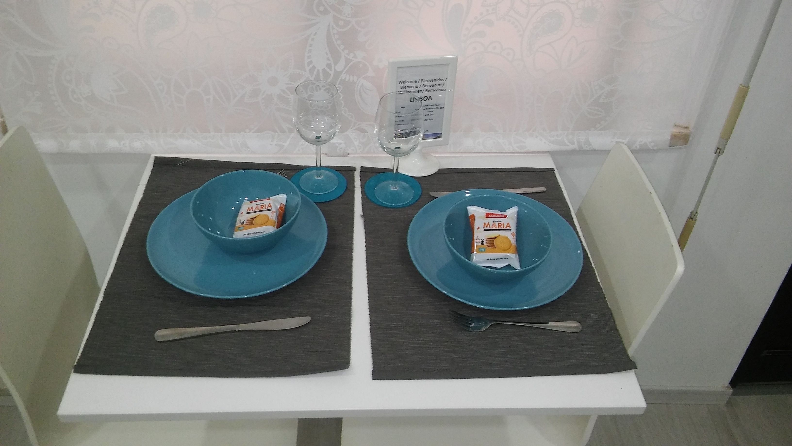 Ein Esstisch mit zwei blauen Tellern, auf jedem ein Packung Maria-Kekse, und zwei Weingläser.