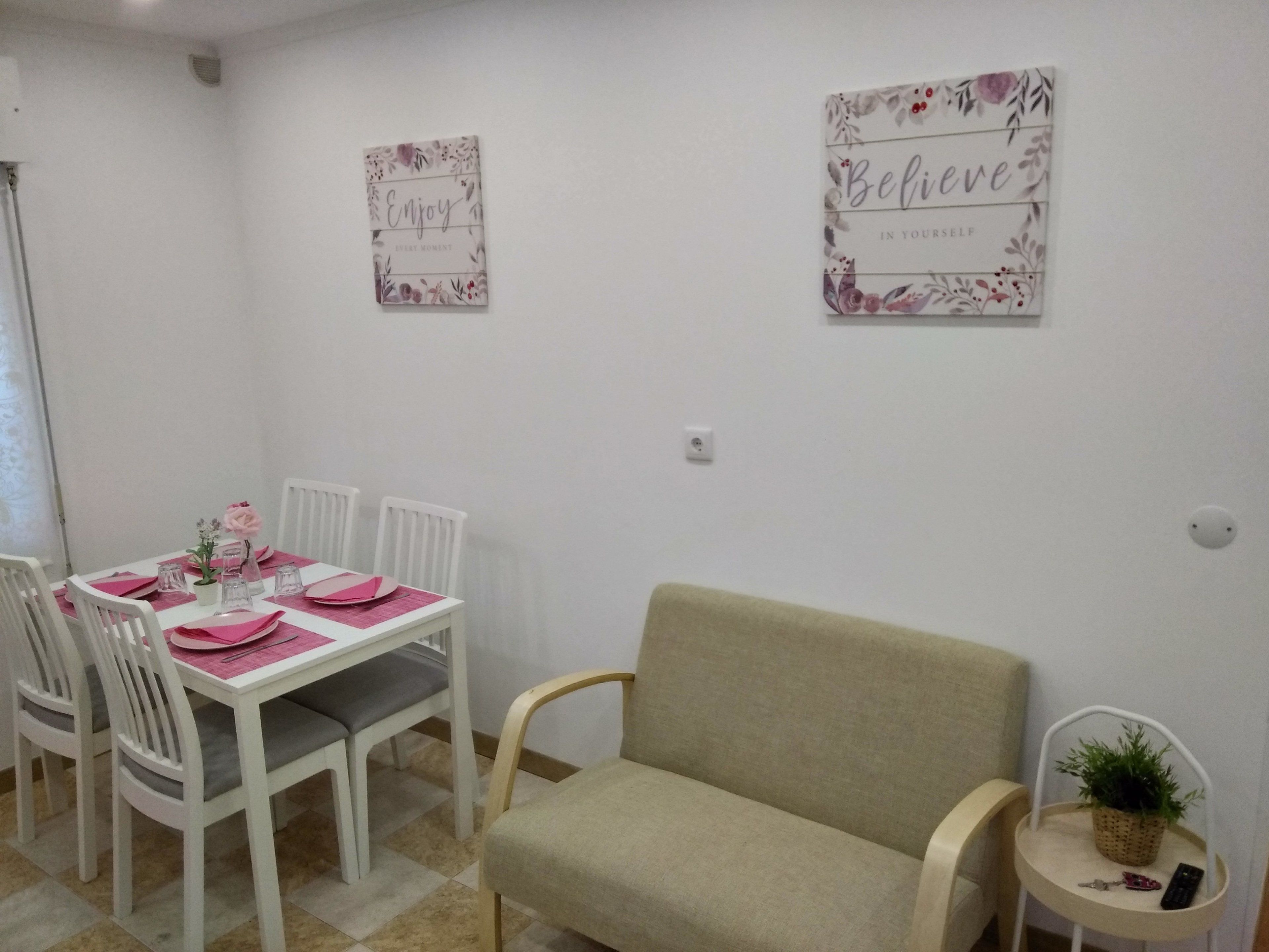 A dining area with a table set for four, white chairs, a beige sofa, and two motivational wall art pieces.