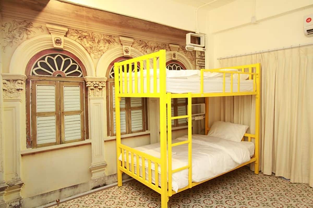 Una habitación con literas, dos ventanas con contraventanas, un suelo estampado y una pared decorativa.
