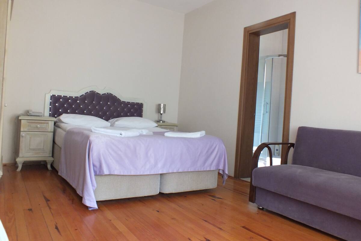 A bedroom with a bed, a nightstand, a dresser, a mirror, and a sofa.