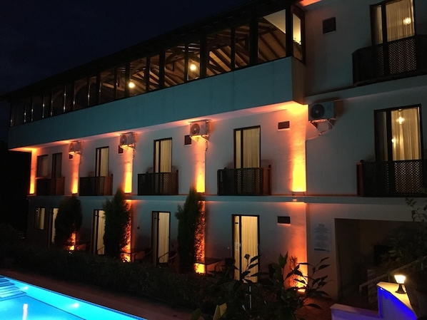 A multi-story hotel with a pool, featuring balconies and warm lighting.