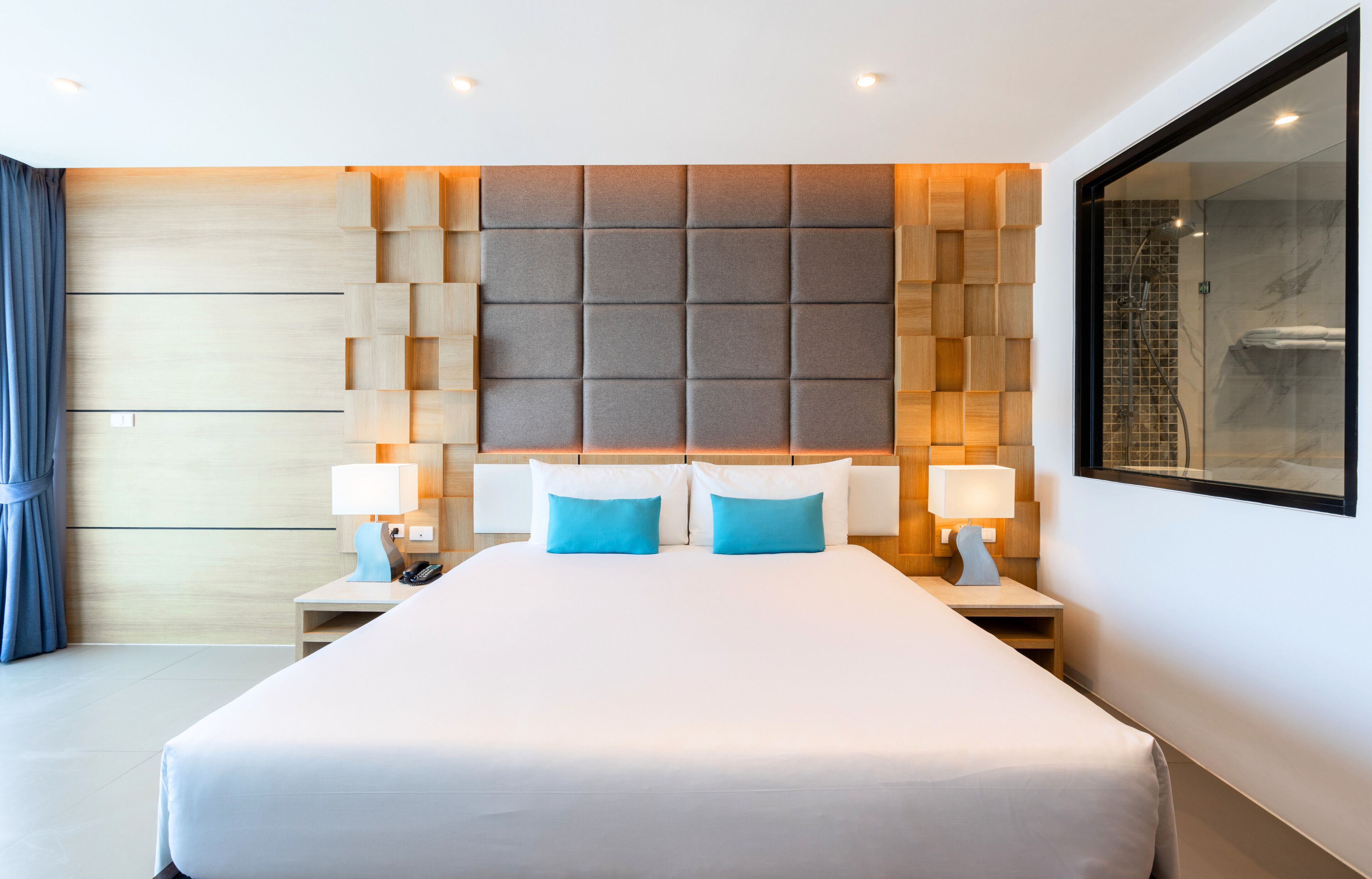 Una habitación de hotel moderna con una cama grande, dos mesitas de noche con lámparas, un cabecero con un diseño geométrico y un espejo grande en la pared.
