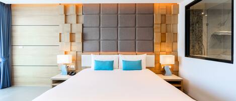 Una habitación de hotel moderna con una cama grande, dos mesitas de noche con lámparas, un cabecero con un diseño geométrico y un espejo grande en la pared.