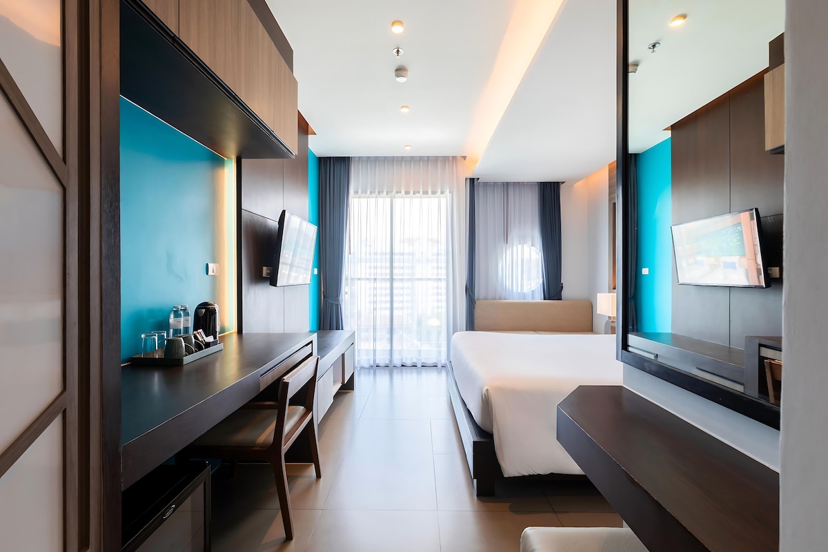 Habitación de hotel con una cama, un escritorio, un televisor y un espejo grande.