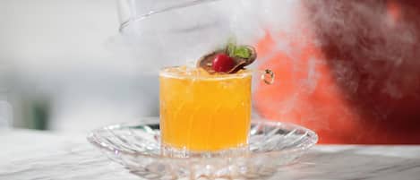 A cocktail with a clear glass dome, a cherry garnish, and a mist effect.