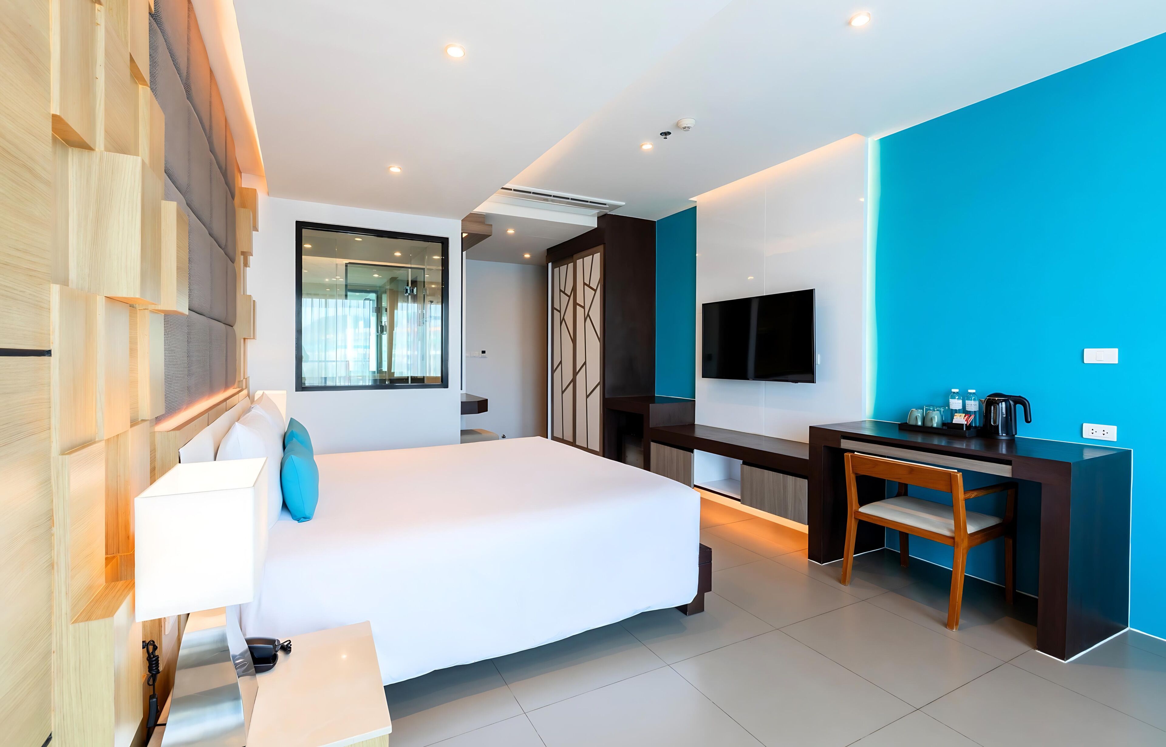 A modern hotel room with a large bed, a desk, a TV, and a view of the city.
