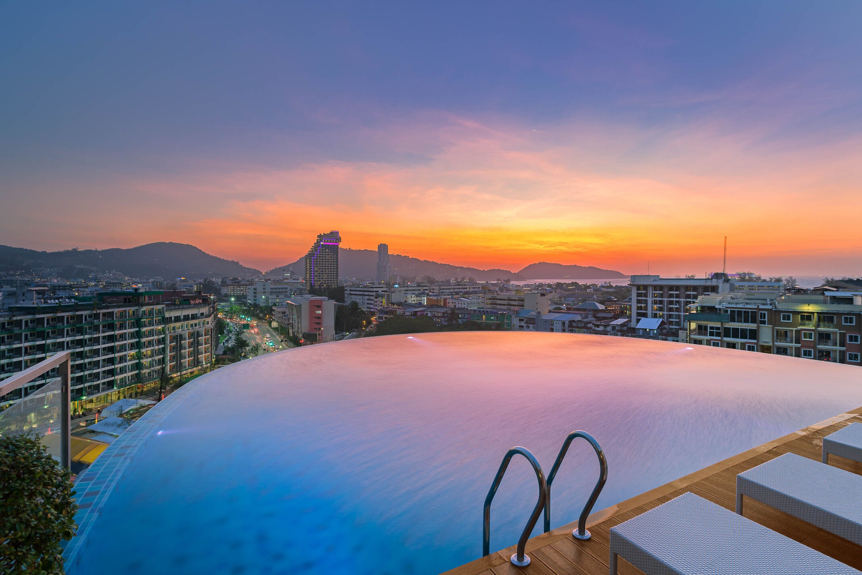 A rooftop infinity pool with a city view at sunset.