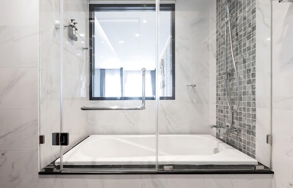 Un baño moderno con ducha de vidrio, una bañera grande y un muro de azulejos con ventana.