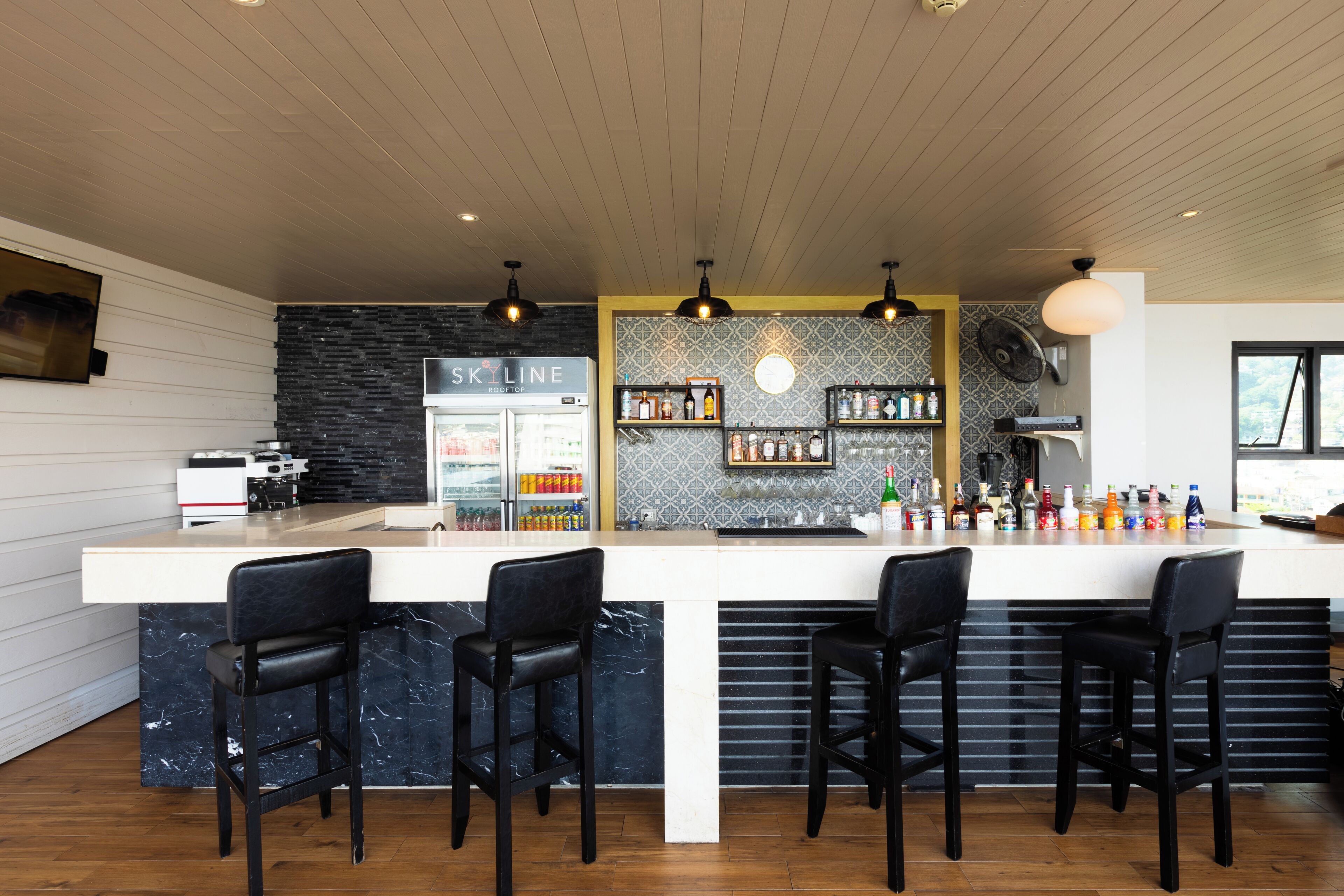 Zona de bar moderna con una barra central, taburetes y una variedad de botellas y vasos en estantes.