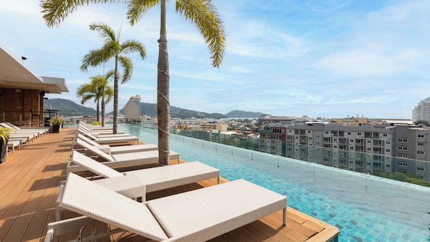 Una piscina a sfioro sul tetto con poltrone relax, palme e vista sulla città.