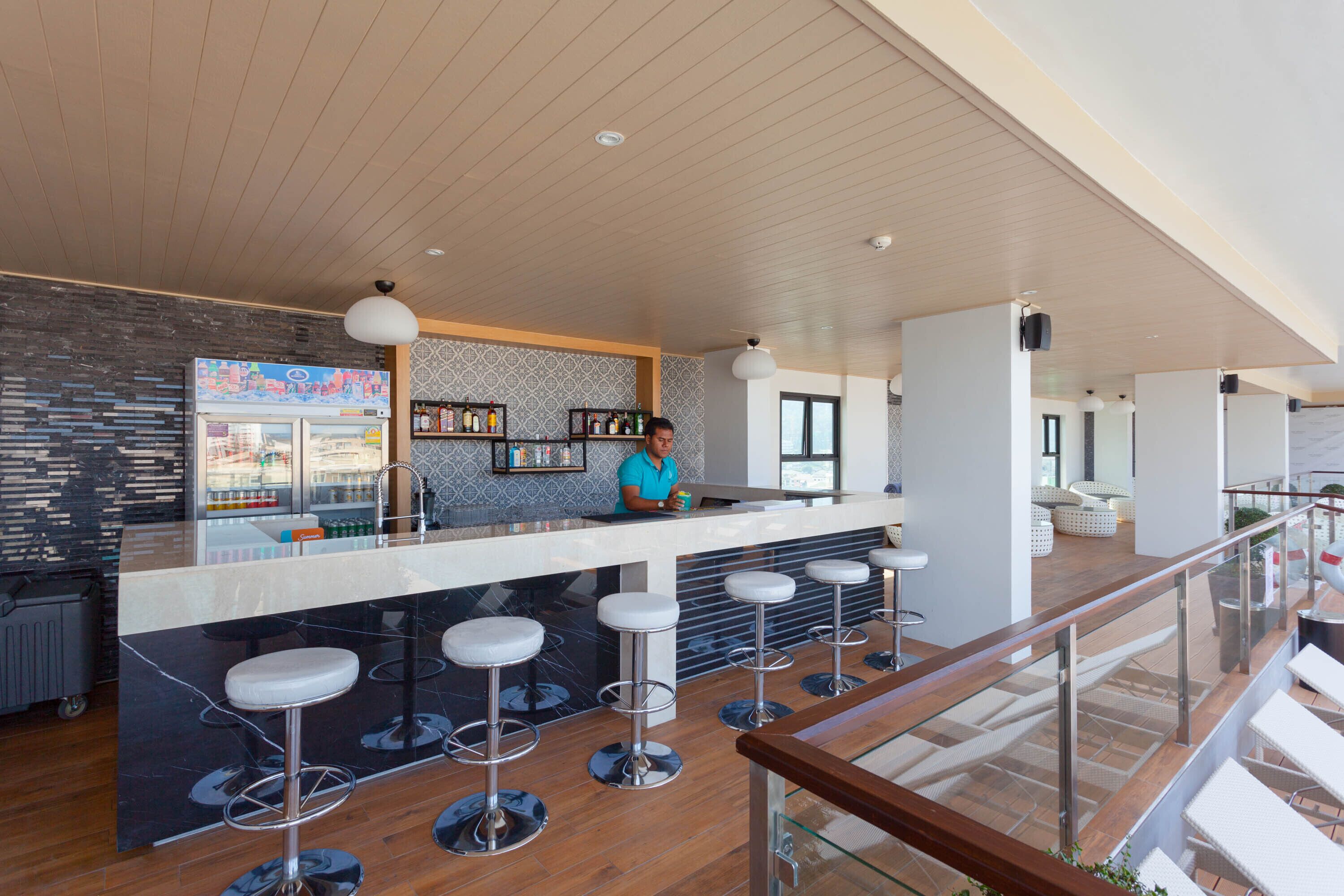 A modern bar area with a counter, stools, and a person standing behind it.