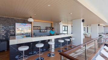 A modern bar area with a counter, stools, and a person standing behind it.