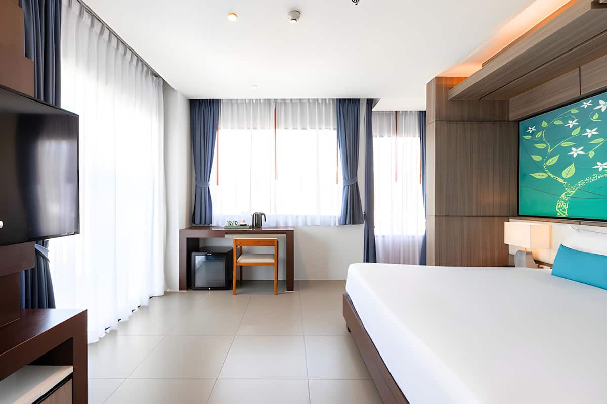 A hotel room with a bed, a desk, a television, and curtains.