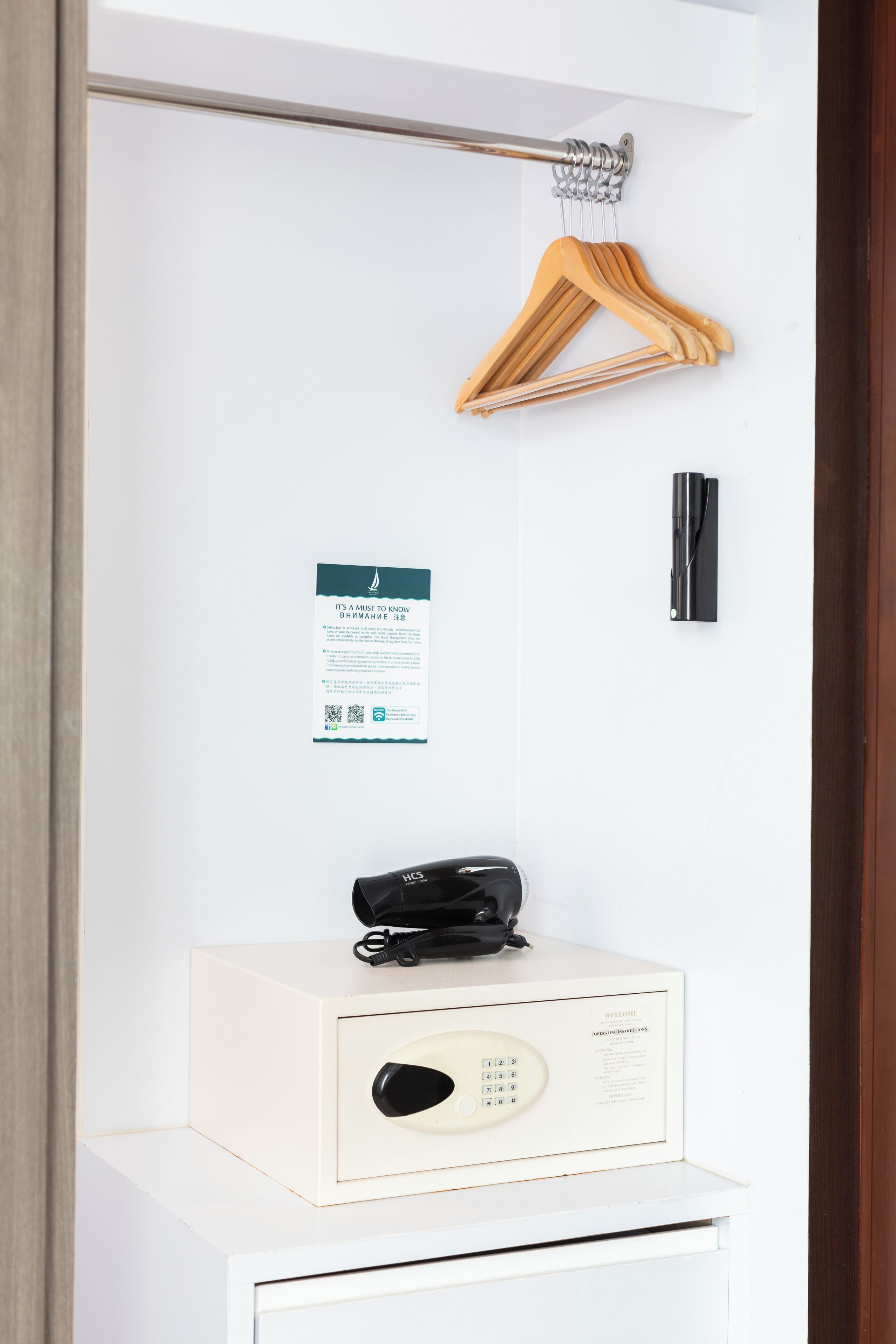 Una habitación con perchero, un cartel con instrucciones de seguridad, un teléfono negro y un armario blanco con teclado.