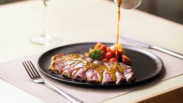 A steak with sauce on a plate, a glass of red wine, and a fork on a table.