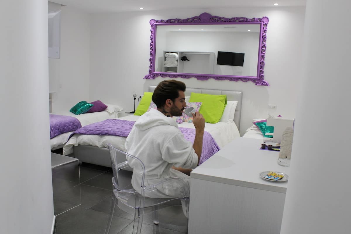 Un dormitorio moderno con cama, escritorio y silla. Hay un espejo sobre la cama y un televisor en la pared.