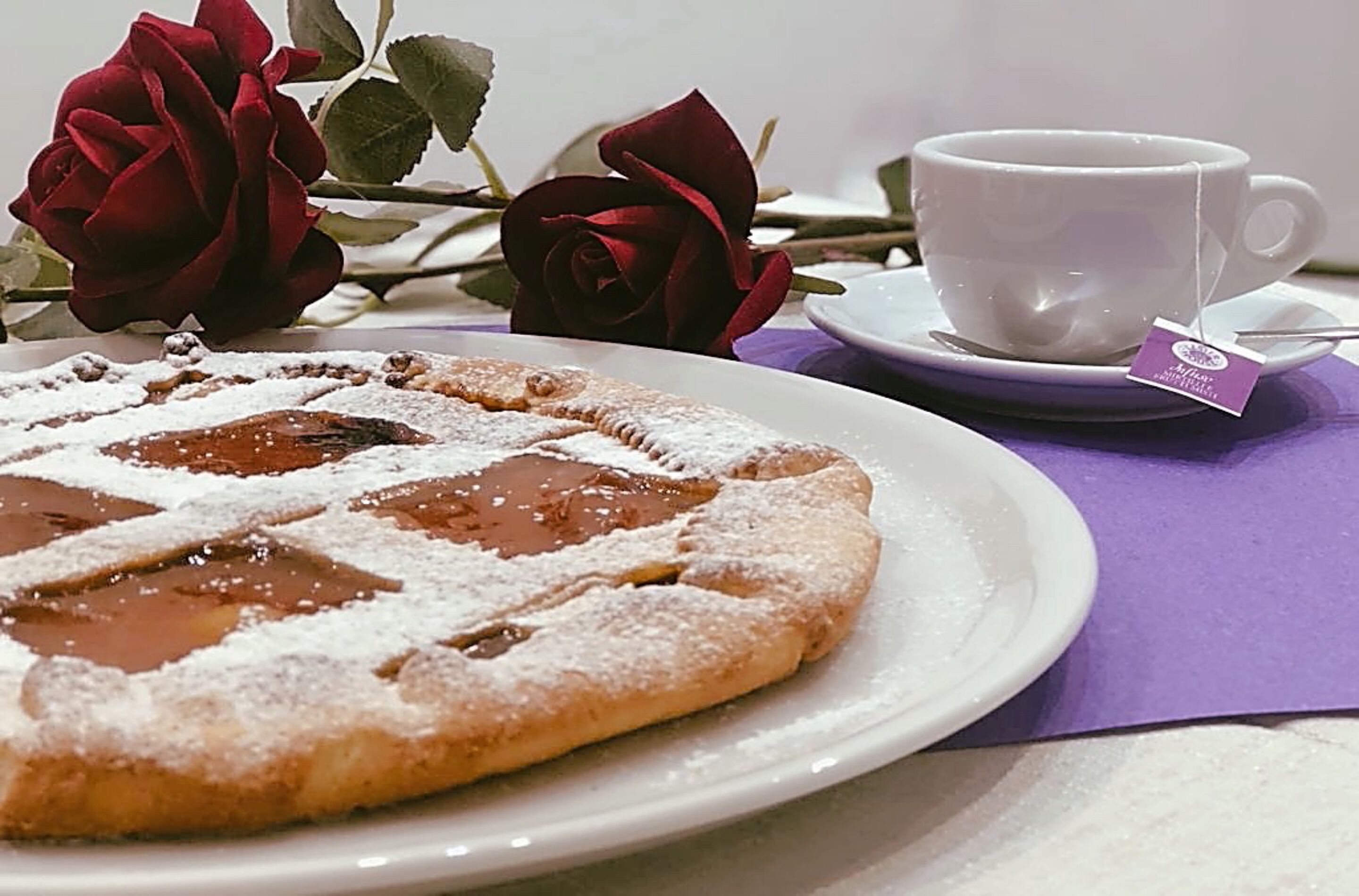 A dessert plate with a pastry, a cup of tea, and roses.