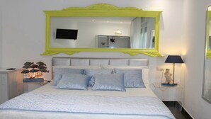 Un dormitorio con una cama grande, un espejo con marco amarillo, una mesita de noche con lámpara y una pequeña estatua.
