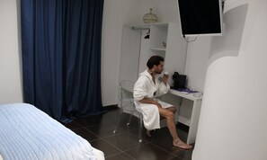 Hotellihuone, jossa on sänky, työpöytä, tuoli, televisio ja kahvinkeitin.