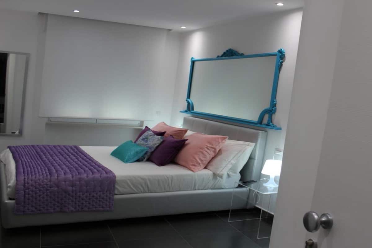 Un dormitorio moderno con cama, almohadas, un espejo de marco azul y una puerta con la etiqueta 'DRAGUT'.