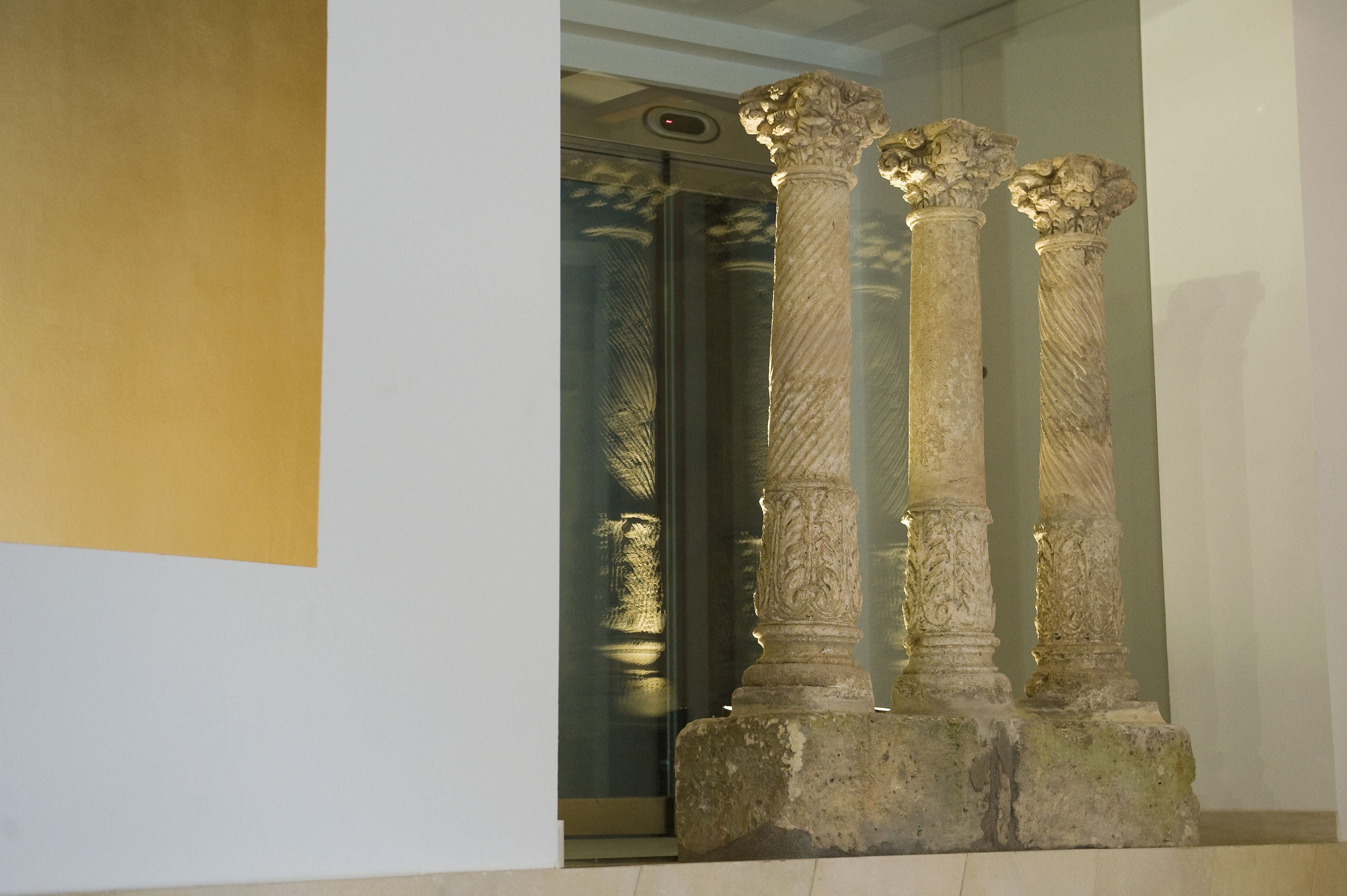 Three ancient columns with intricate carvings, positioned in a well-lit indoor space.