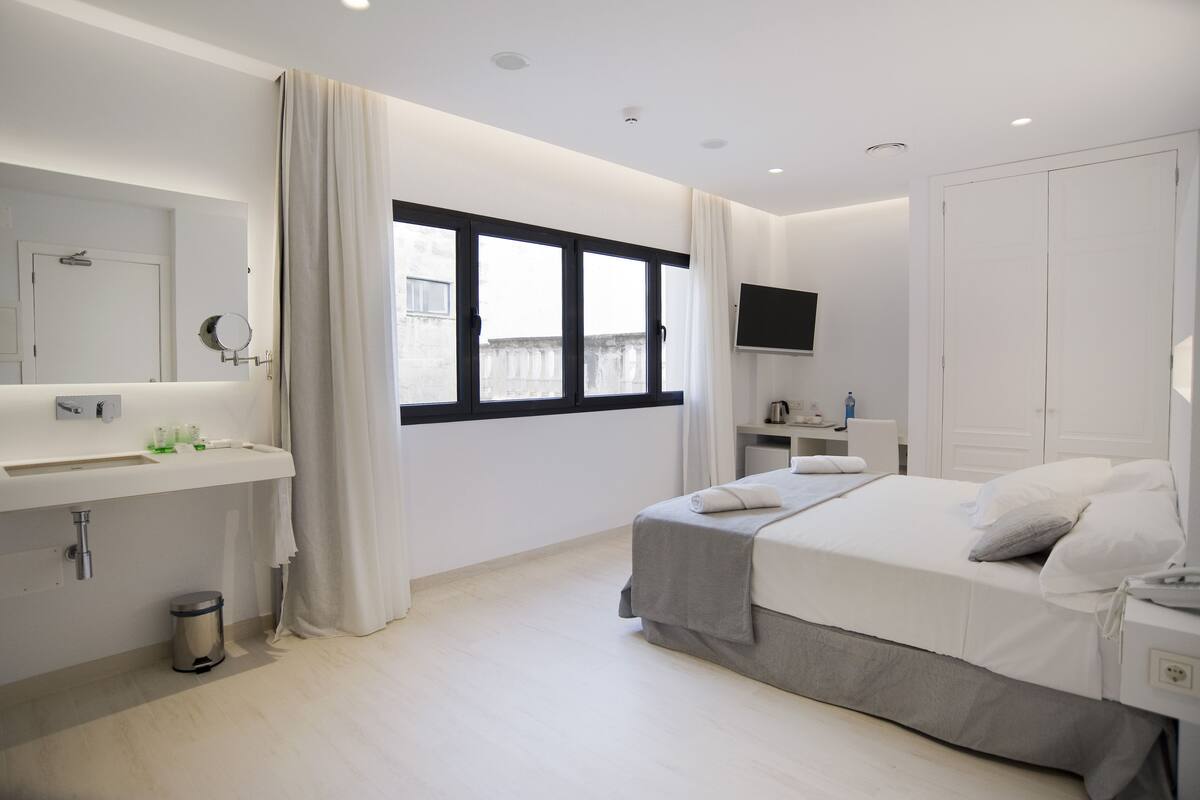Une chambre à coucher moderne avec un lit, une table de chevet, un téléviseur et une fenêtre avec des rideaux.
