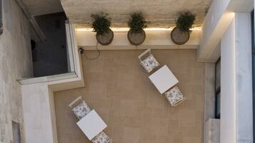 A rooftop terrace with three potted plants, two white tables, and a view of the surrounding area.