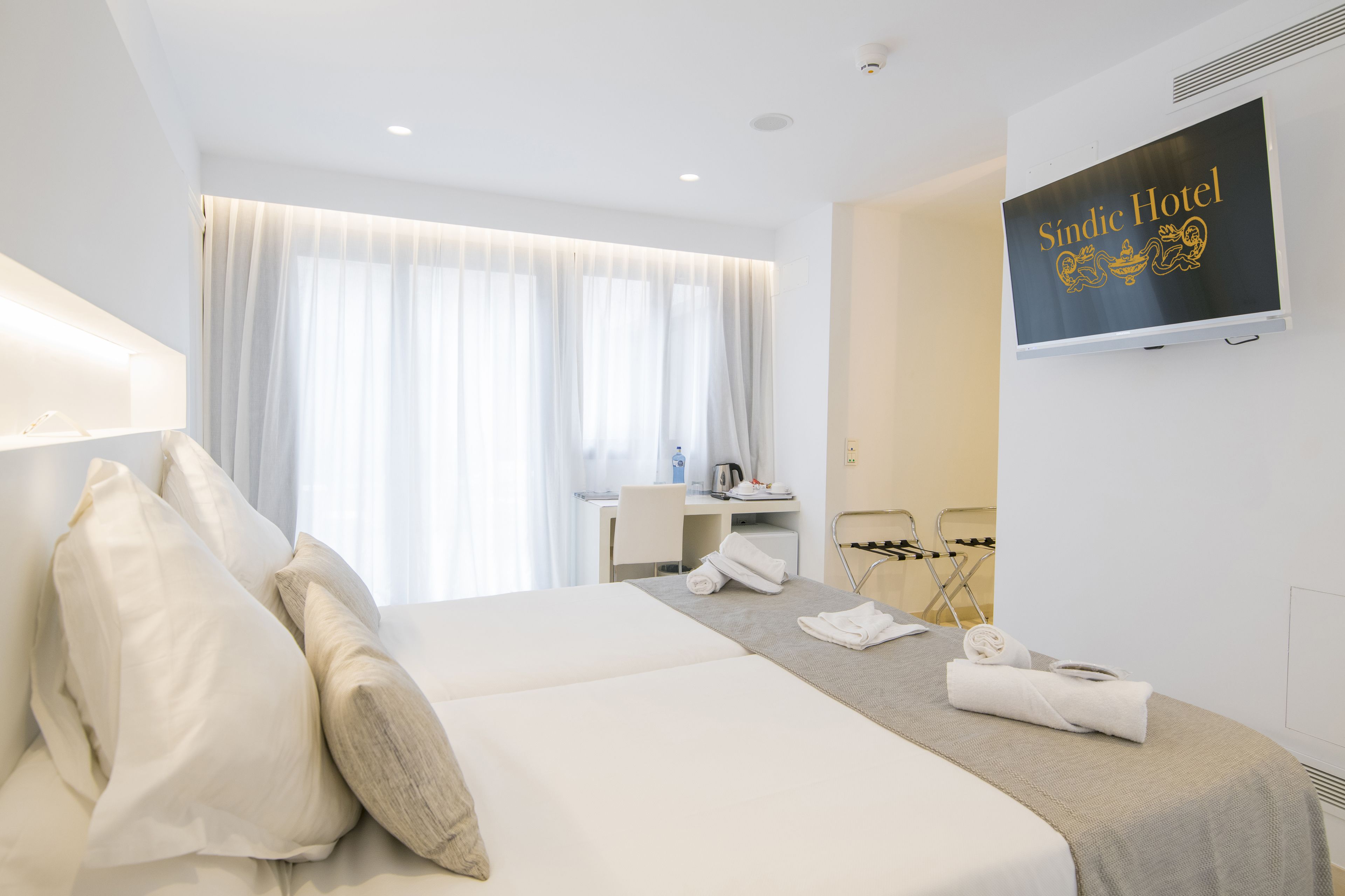 Habitación de hotel con cama, escritorio, silla y televisor mostrando el nombre del hotel.