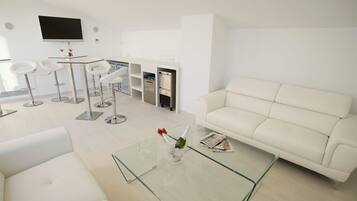 Uma sala de estar moderna com um sofá branco, mesa de centro de vidro e uma TV na parede.
