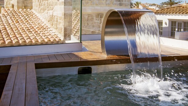 A modern building with a water feature, a wooden deck, and a clear sky. - Sindic Hotel - Adults Only (Mahón)