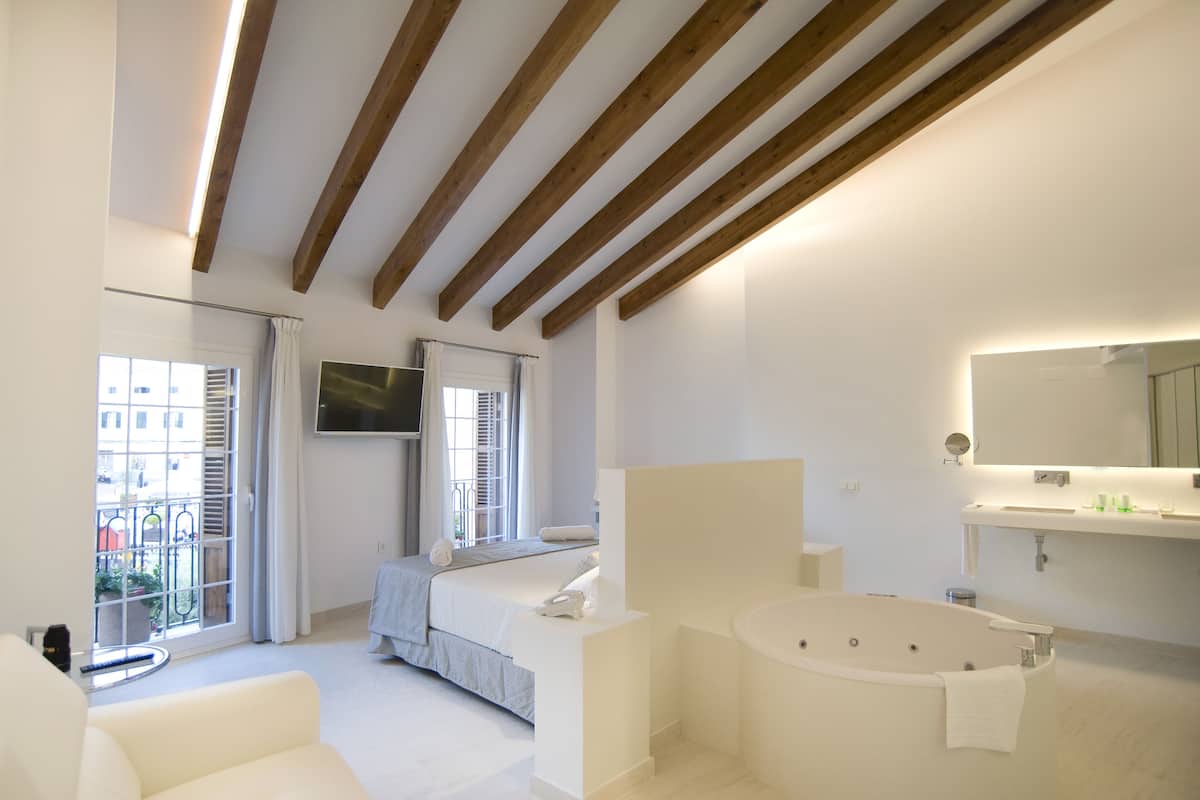 Une chambre moderne dotée d’un grand lit, d’un coin salon, d’un balcon et d’une salle de bain avec une baignoire et un grand miroir.