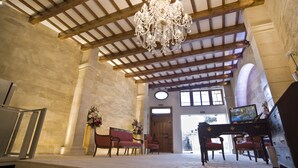 A spacious lobby with a high ceiling, wooden beams, and a chandelier. There are seating areas with red upholstered chairs and a piano. - Sindic Hotel - Adults Only (Mahón)