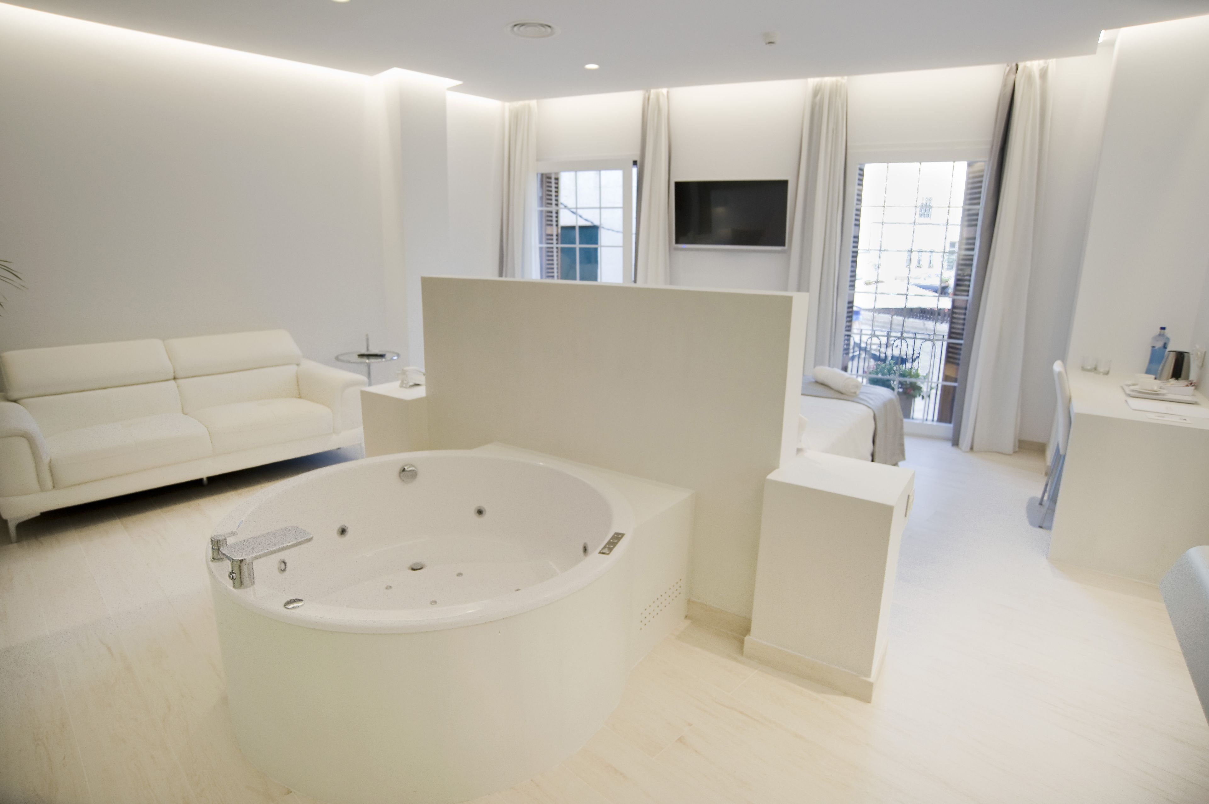 A modern, minimalist bathroom with a large bathtub, a sofa, and a TV mounted on the wall.