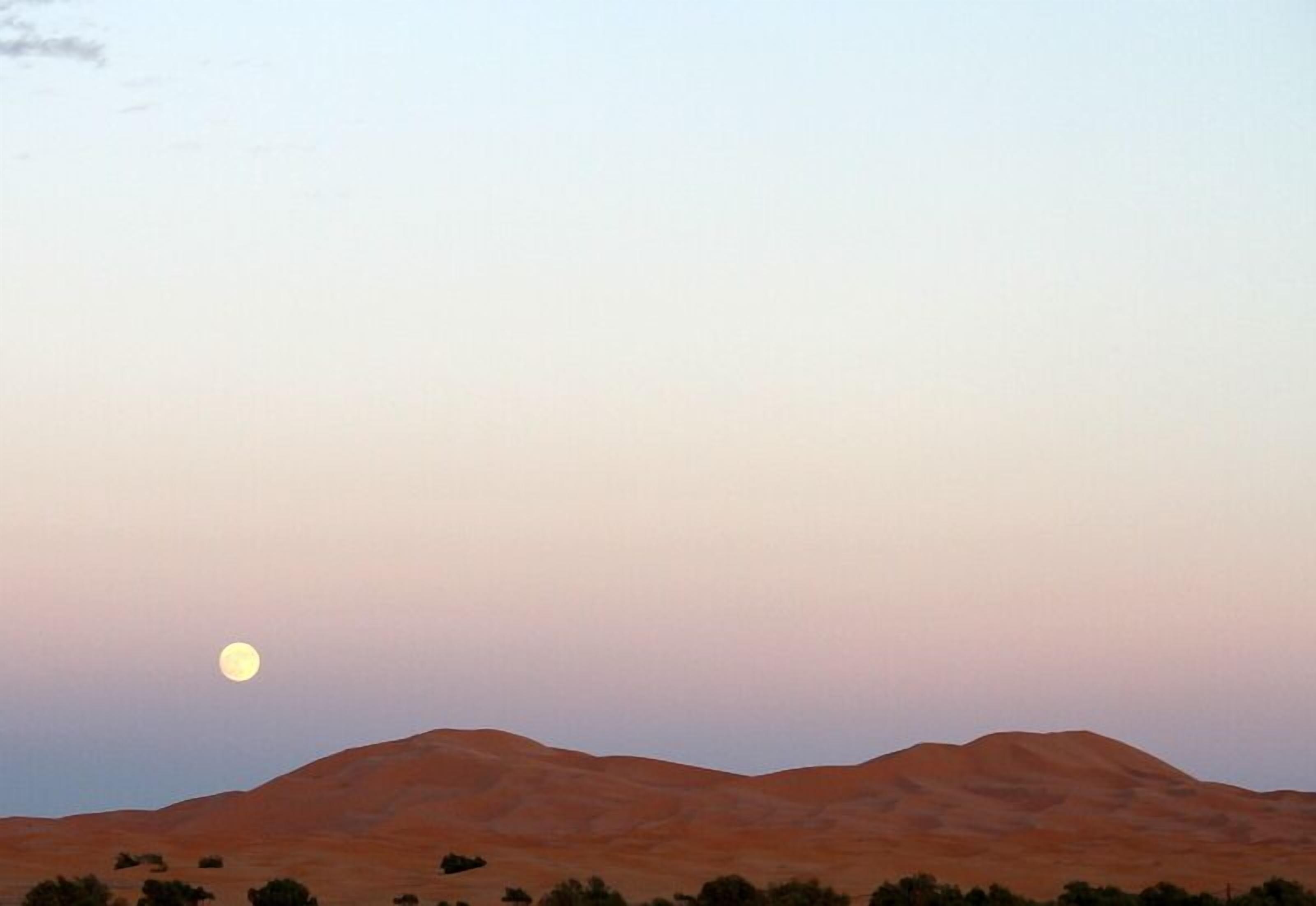 Paisaje desértico con una colina destacada y una luna llena en el cielo.